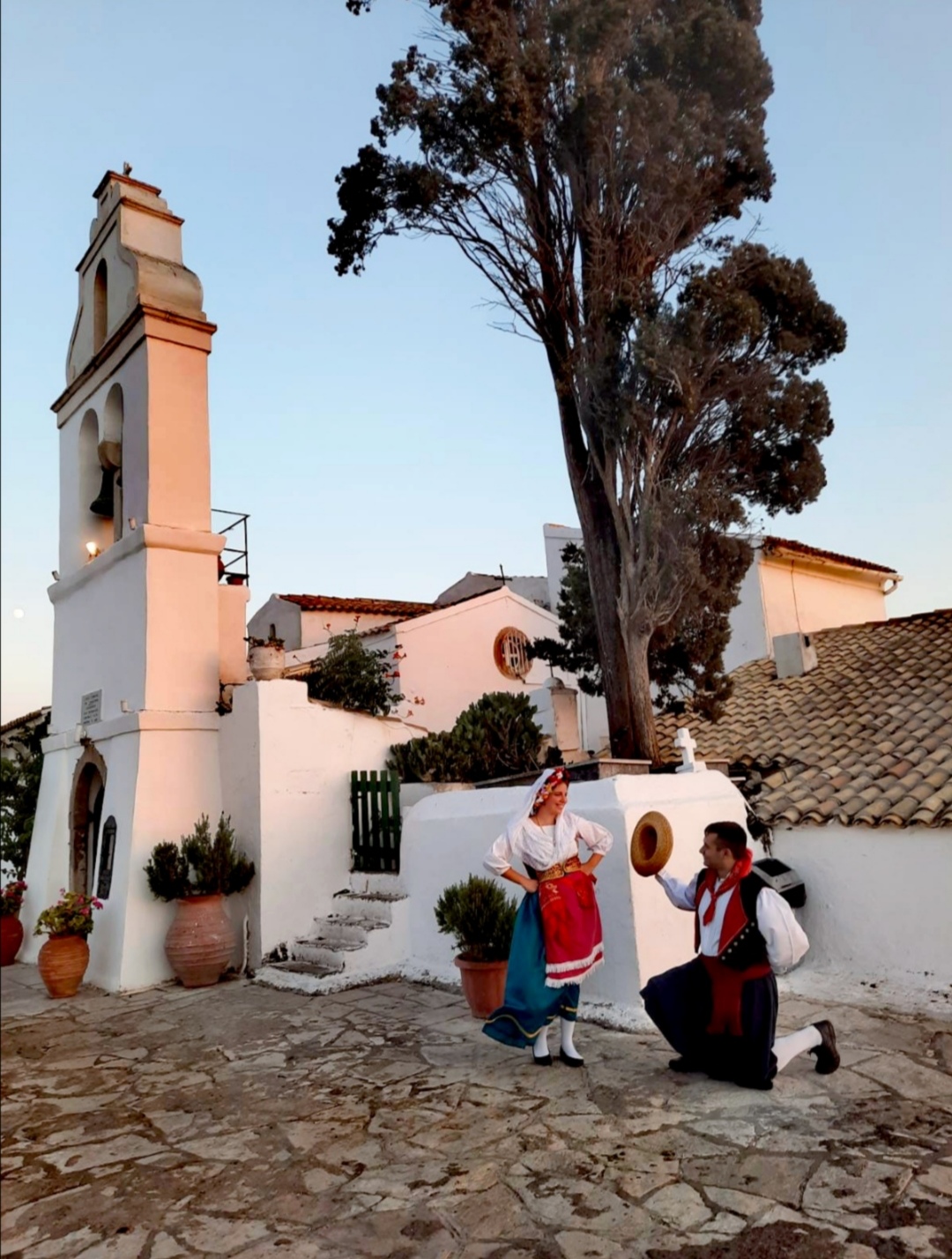 A couple in Corfiot costume in a doorway, with a courtyard behind them.