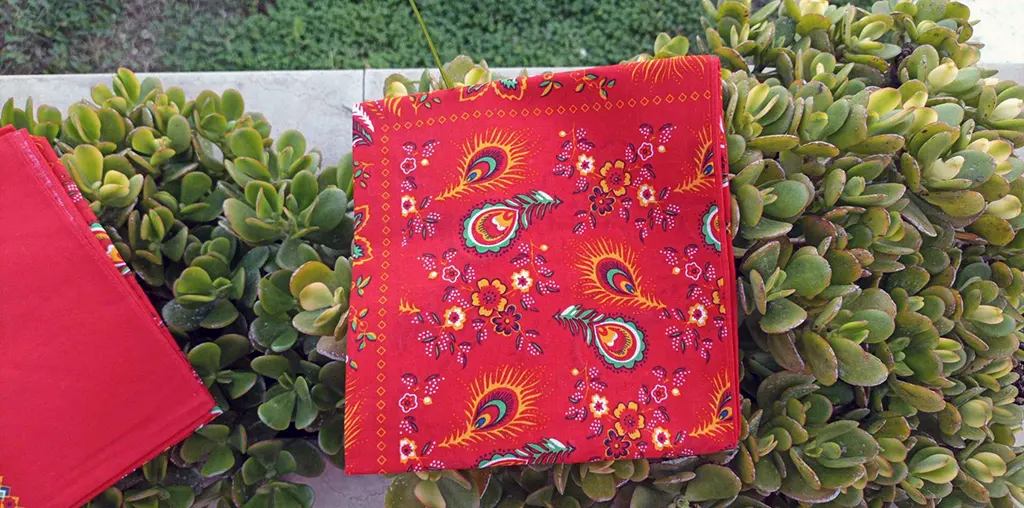 A folded red tsoutsoumida, printed with peacock feathers and flowers.